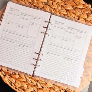 May include: Open planner with Character Study pages. The pages are white with black text and lines for writing. The planner is open on a woven, light brown surface.