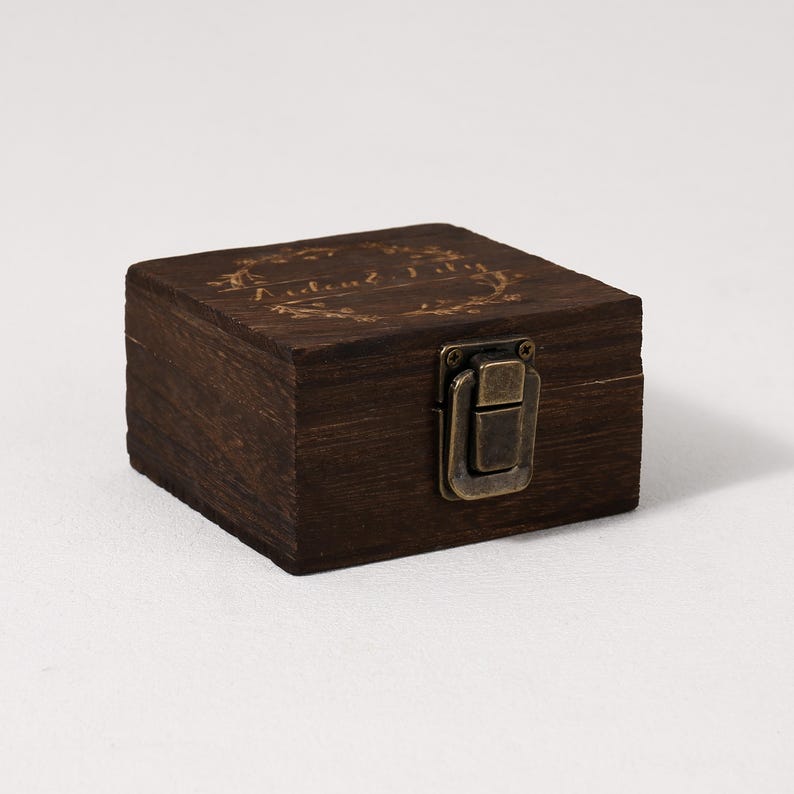 May include: A small, dark brown wooden box with a brass latch. The box has a floral design and the words "Andrew & Jill" engraved on the top.