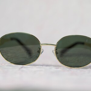 Puede incluir: Un par de gafas de sol redondas con montura dorada y lentes verde oscuro.