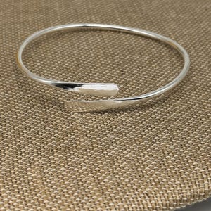 May include: A silver bangle bracelet with a unique twist design. The bracelet is made of a thin, smooth metal and has a simple, elegant look.