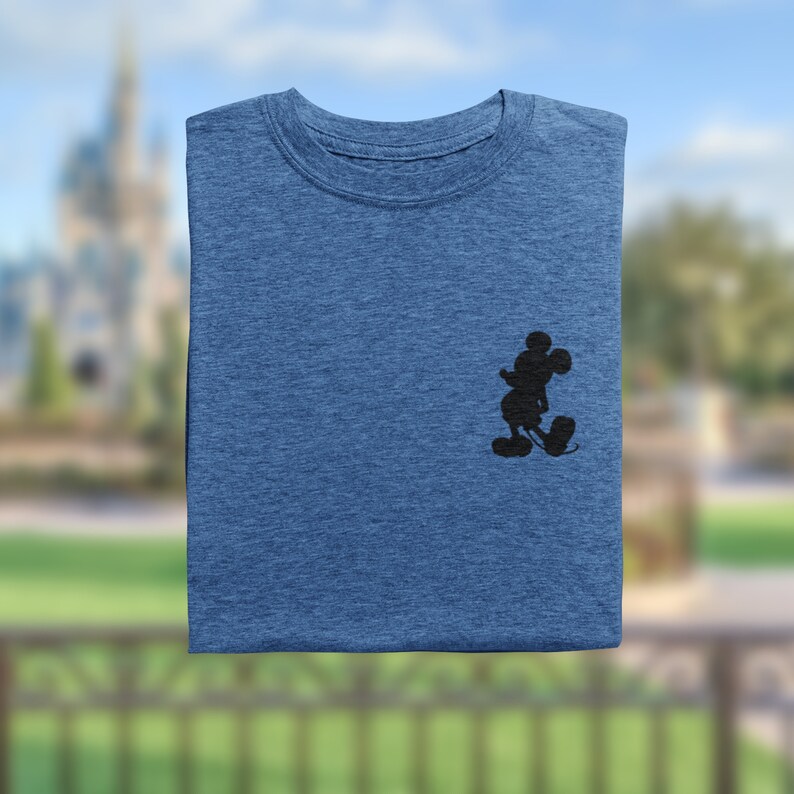 Puede incluir: Una camiseta azul doblada con una silueta negra de Mickey Mouse en el lado izquierdo del pecho.