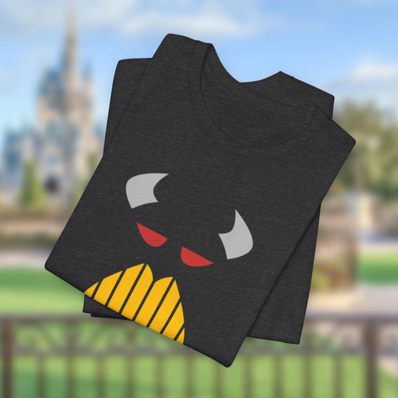 Puede incluir: Una camiseta negra con un gr&aacute;fico de un monstruo de dibujos animados con ojos rojos, cuernos blancos y una boca rayada amarilla y negra.
