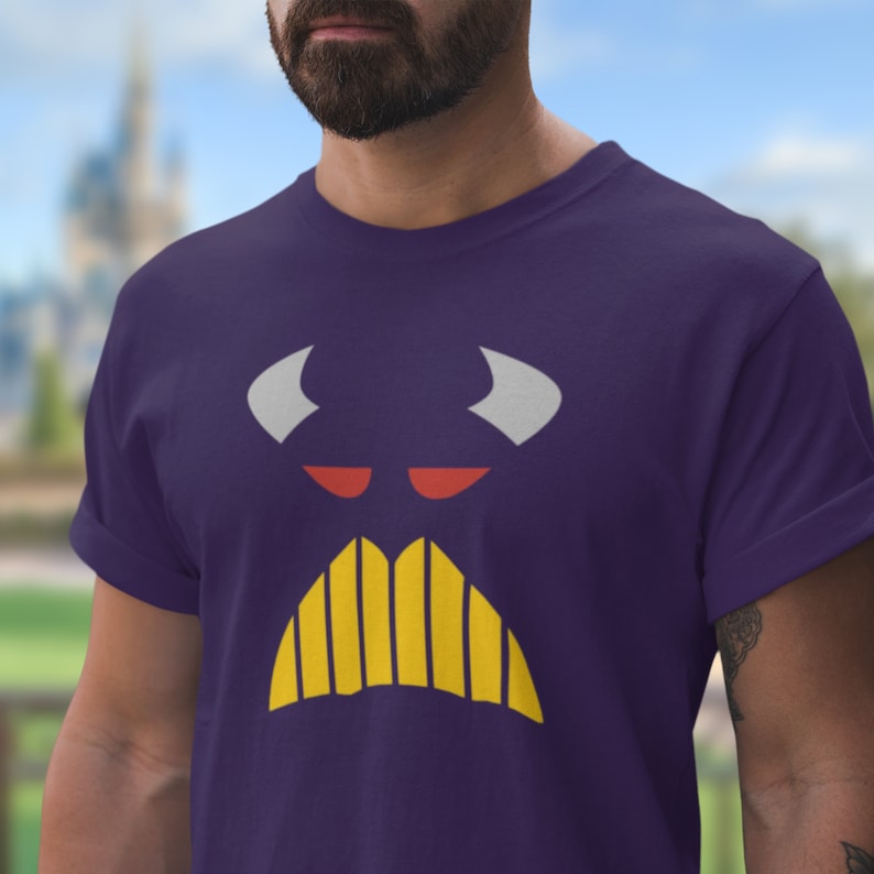 Puede incluir: Camiseta morada con un gr&aacute;fico de cara de dibujos animados. La cara tiene cuernos blancos, ojos rojos y un bigote amarillo.
