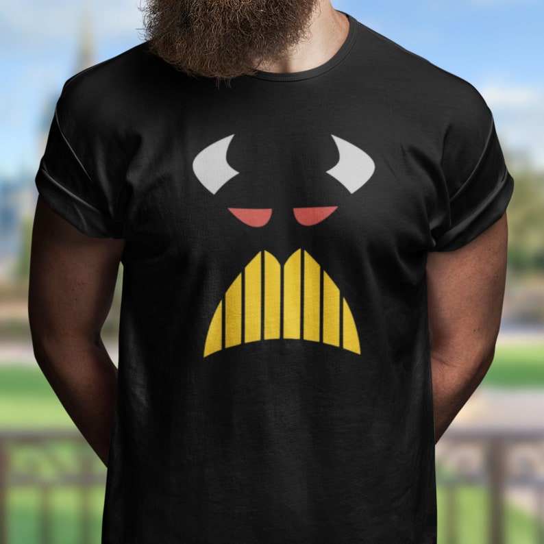 Puede incluir: Camiseta negra con un gr&aacute;fico blanco y amarillo de una cara con cuernos y bigote.