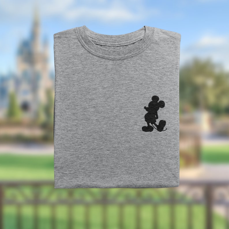 Puede incluir: Una camiseta gris con una silueta negra de Mickey Mouse en el lado izquierdo del pecho.