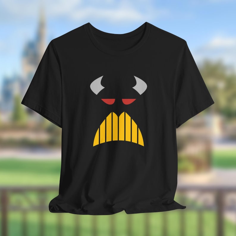 Puede incluir: Camiseta negra con un gr&aacute;fico blanco y amarillo de una cara con cuernos y bigote.