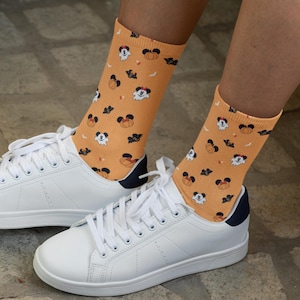 May include: A pair of orange socks with a Halloween-themed print featuring Mickey Mouse, pumpkins, and bats. The socks are worn with white sneakers.