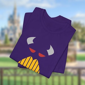 Puede incluir: Camiseta morada con un gr&aacute;fico de cara de monstruo de dibujos animados. El monstruo tiene ojos rojos, cuernos blancos y una boca amarilla y naranja.