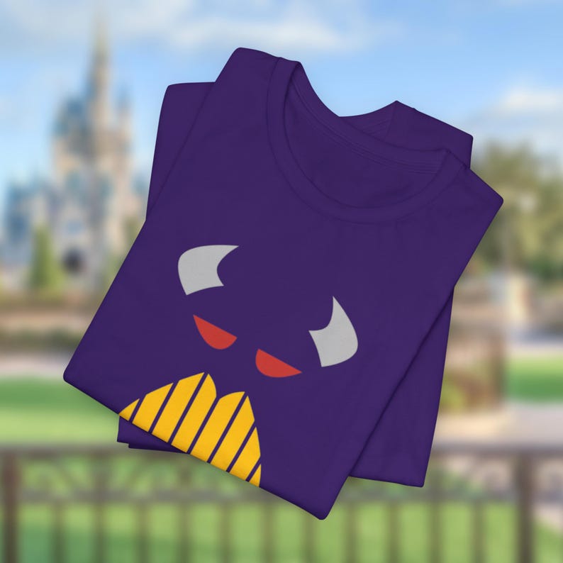 Puede incluir: Camiseta morada con un gr&aacute;fico de cara de monstruo de dibujos animados. El monstruo tiene ojos rojos, cuernos blancos y una boca amarilla y naranja.