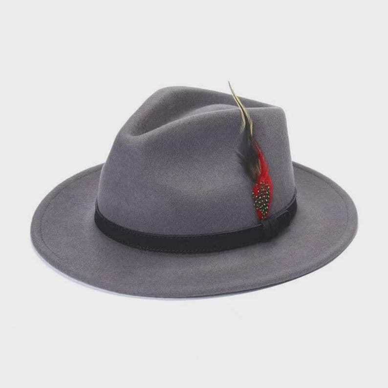 Peut inclure: Un chapeau fedora gris avec un bandeau noir et une plume d&eacute;corative. Le chapeau a un design classique avec un large bord et une couronne pinc&eacute;e. La plume est rouge, noire et jaune.