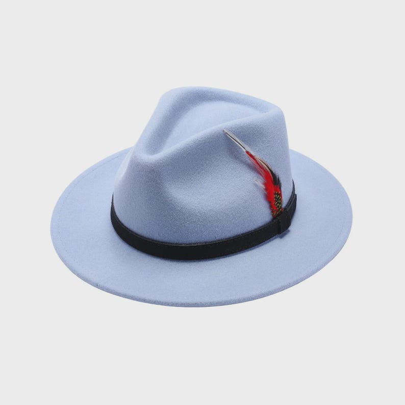 Peut inclure: Un chapeau fedora bleu clair avec un bandeau noir et une plume d&eacute;corative. Le chapeau a un bord classique l&eacute;g&egrave;rement inclin&eacute; et une texture douce semblable &agrave; du feutre. La plume est rouge et noire.