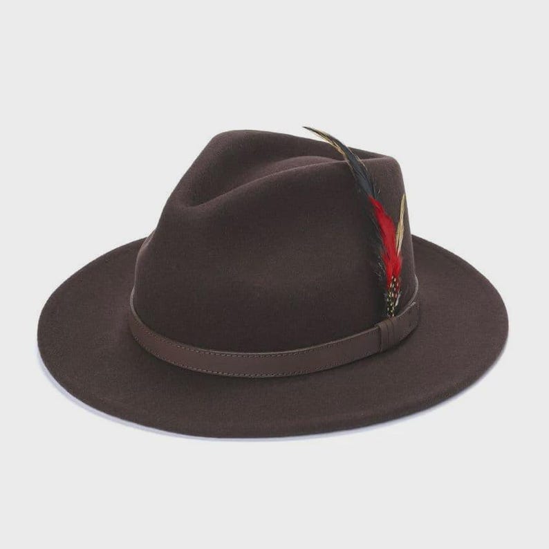 Peut inclure: Un chapeau fedora marron fonc&eacute; avec un bandeau en cuir et une plume d&eacute;corative. Le chapeau a un large bord et une forme classique. La plume est rouge, noire et jaune.