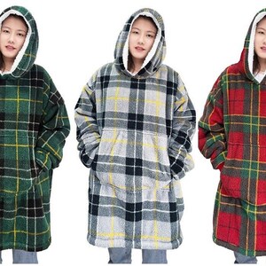 May include: Three oversized hooded blankets with plaid patterns in green, grey, and red. The blankets have large pockets and are made of soft, plush fabric.