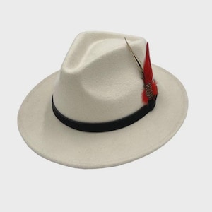 Peut inclure: Un chapeau fedora cr&egrave;me avec une bande noire et une plume rouge d&eacute;corative. Le chapeau a une forme classique et structur&eacute;e avec un large bord. La plume ajoute une touche de couleur et de style au chapeau.