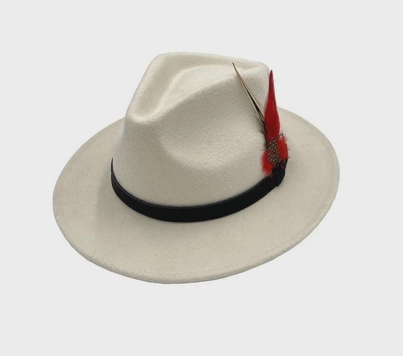 Peut inclure: Un chapeau fedora cr&egrave;me avec une bande noire et une plume rouge d&eacute;corative. Le chapeau a une forme classique et structur&eacute;e avec un large bord. La plume ajoute une touche de couleur et de style au chapeau.