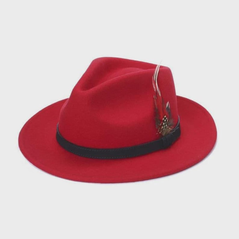 Peut inclure: Un chapeau fedora rouge vif avec une bande noire et une plume d&eacute;corative. Le chapeau a un bord classique et une couronne structur&eacute;e. Ce chapeau &eacute;l&eacute;gant est un accessoire de mode.