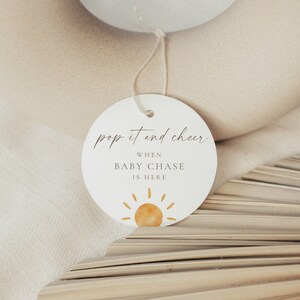 Puede incluir: Etiqueta redonda blanca con el texto "pop it and cheer" y "when baby chase is here" con una ilustración de sol amarillo.