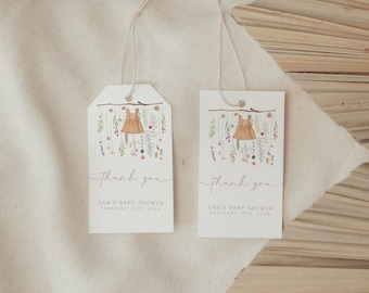 Puede incluir: Dos etiquetas blancas de agradecimiento con una ilustración de acuarela de un vestido colgado de una rama con flores y vegetación. El texto en las etiquetas dice "Gracias" y "Baby Shower de Sam, 13 de febrero de 20XX".