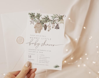 Könnte beinhalten: Eine Babyparty-Einladung mit einer Aquarellillustration von Babykleidung und Kiefernzweigen. Die Einladung lautet "Merry Little Baby Shower" und enthält Details zur Veranstaltung. Die Einladung wird von einer Person gehalten.