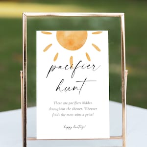May include: A white sign with a yellow sun graphic and the text "pacifier hunt". The sign says "There are pacifiers hidden throughout the shower. Whoever finds the most wins a price! happy hunting!"