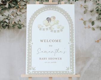 May include: Welcome to Samantha's Baby Shower sign with a watercolor illustration of a couple sleeping on a cloud with a banner of flags. The sign is on a wooden easel against a green leafy background.