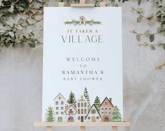 May include: A white rectangular welcome sign on a wooden easel featuring a watercolor illustration of a village with houses and pine trees. The text reads IT TAKES A VILLAGE WELCOME TO SAMANTHA'S BABY SHOWER in dark brown lettering.