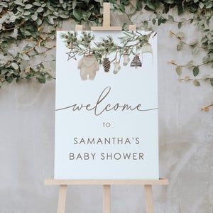 May include: Welcome to Samantha's Baby Shower sign featuring a watercolour illustration of a pine branch with decorations including a baby onesie, a pine cone, a sock, a stocking, and a small Christmas tree.