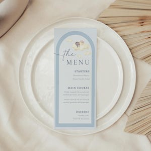 May include: A blue and white menu card with an illustration of two figures on clouds. The text "The Menu" is written in a script font. The menu includes sections for starters, main course, and dessert.