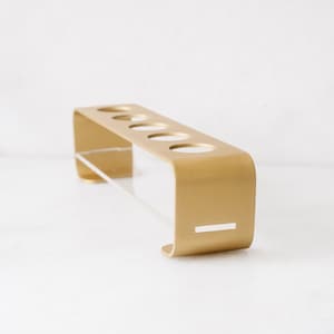 May include: Gold metal toothbrush holder with five slots and a clear acrylic base.