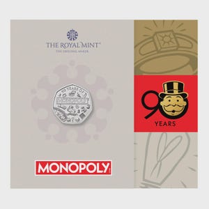 May include: A commemorative coin celebrating 90 years of Monopoly, featuring the game's iconic elements. The coin is displayed on a light gray background with the Royal Mint logo and the Monopoly logo in red.