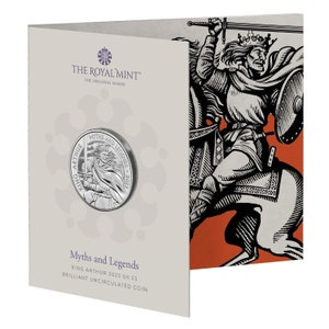 May include: A silver coin featuring King Arthur holding a sword and shield. The coin is presented in a cardboard folder with a black and white illustration of King Arthur on horseback. The coin inscription reads "King Arthur, Myths and Legends, 2023".