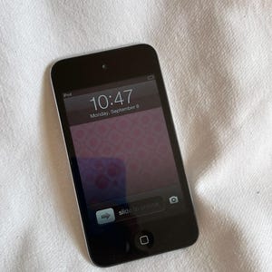 以下が含まれることがあります： 黒いiPod touch、シルバーの縁取り、10:47と9月8日（月）の日付が表示されたロック画面を表示。画面にはピンクの花柄が表示されています。「スライドしてロック解除」のテキストが表示されています。