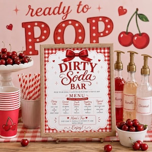 Op de afbeelding: Een ingelijst Dirty Soda Bar menubord met rood-witte vichy-ruitranden, een rode strik en tekst met frisdrankcombinaties. De display bevat rood-wit gestreepte papieren rietjes, rode bekers met kersenafbeeldingen en glazen siroopflessen.