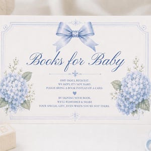 Puede incluir: Un letrero de baby shower con el texto "Books for Baby". El letrero presenta un lazo azul claro, detalles florales y una solicitud de libros en lugar de tarjetas. El letrero está rodeado de artículos para bebés.