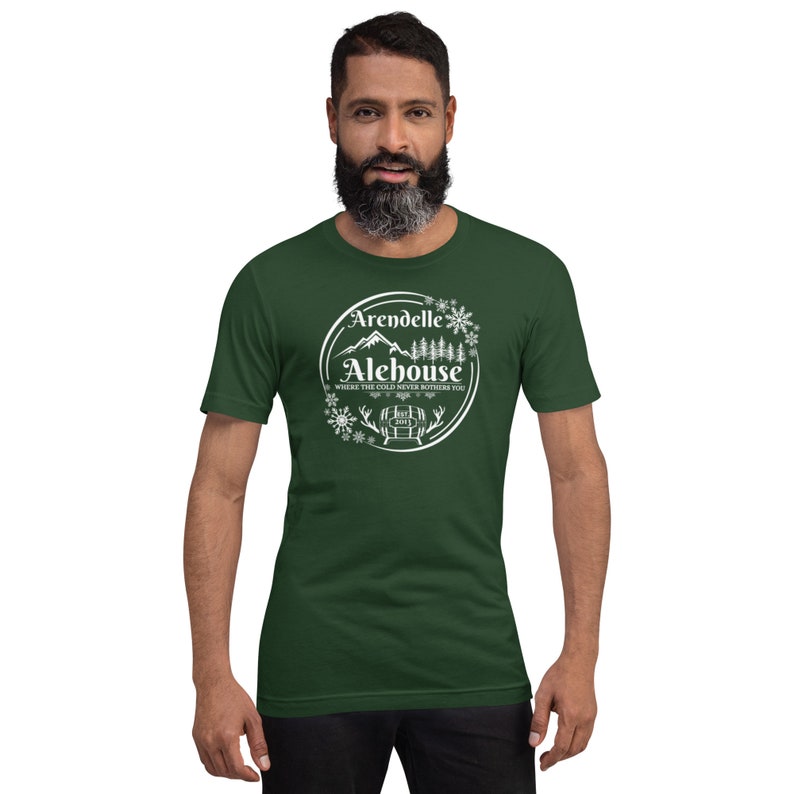 May include: A green t-shirt with a white circle design featuring the text "Arendelle Alehouse" and a mountain scene with snowflakes. The text below the logo reads "Where the cold never bothers you".