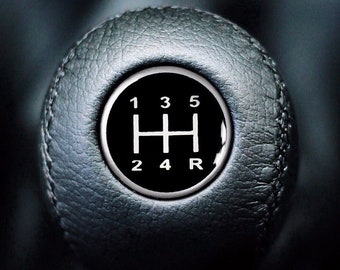 Può includere: Un pomello del cambio in pelle nera con uno schema di cambio in argento. Lo schema include i numeri 1, 2, 3, 4, 5 e R.