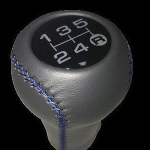 May include: Gray leather gear shift knob with blue stitching and a black gear pattern with the numbers 1, 2, 3, 4, 5 and the letter F.