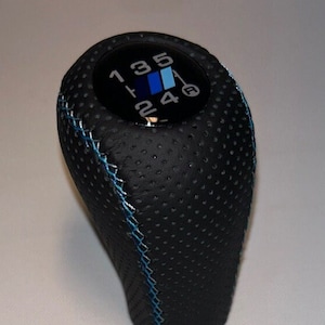 May include: Black leather gear shift knob with blue stitching and a black and blue gear shift pattern with the numbers 1, 2, 3, 4, 5, and R.