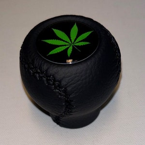 May include: Black leather gear shift knob with a green marijuana leaf design.