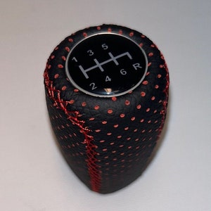 Può includere: Pomello del cambio in pelle nera con cuciture rosse e uno schema di marcia argentato con i numeri 1, 2, 3, 4, 5, 6 e R.