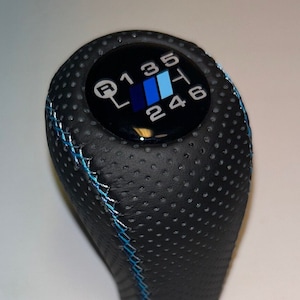Può includere: Pomello del cambio in pelle nera con cuciture blu e bianche e uno schema di cambio nero e blu con i numeri 1, 3, 5, R, H, 2, 4 e 6.