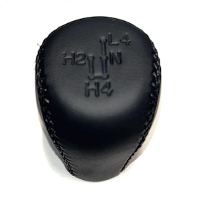 May include: Black leather gear shift knob with stitched edges. The top of the knob has embossed markings: H2, L4, N, and H4, indicating gear positions. The knob is designed for a vehicle's transmission.