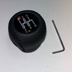 May include: Black leather gear shift knob with a black and silver gear shift pattern. The pattern includes the numbers 1, 2, 3, 4, 5, and R. A silver Allen wrench is included.