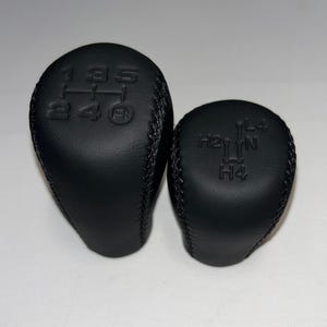 Può includere: Due pomelli del cambio in pelle nera. Uno è più grande con i numeri 1, 2, 3, 4 e 5, più R. L'altro è più piccolo con i contrassegni H2, H4, L4 e N.
