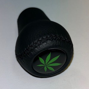 May include: Black leather gear shift knob with a green cannabis leaf design.
