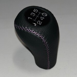 May include: Black leather gear stick knob with purple stitching. The top shows the gear shift pattern: 1, 3, 5, R, 2, 4. The knob is designed for a manual transmission.