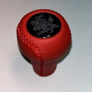 May include: Red leather gear shift knob with a black circular emblem featuring a silver knight on horseback and the word "LITHUANIA".