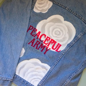 May include: A blue denim jacket with white painted roses and the words "PEACEFUL ARMY" in red lettering.