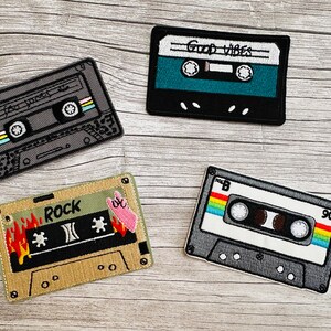 Könnte beinhalten: Vier gestickte Kassetten-Patches mit verschiedenen Designs. Die Patches sind schwarz, grau, beige und türkis. Die Designs beinhalten die Wörter "Rock", "Good Vibes" und "90".