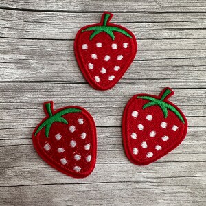 Könnte beinhalten: Drei rote Filz-Erdbeer-Patches mit weißen Punkten und grünen Blättern.